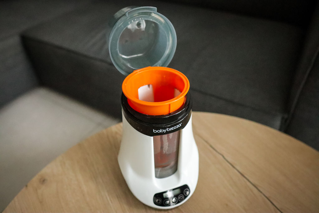A photo of the Baby Brezza Smart Baby Bottle Warmer with the lid opened and the orange tray visible in the warming chamber.