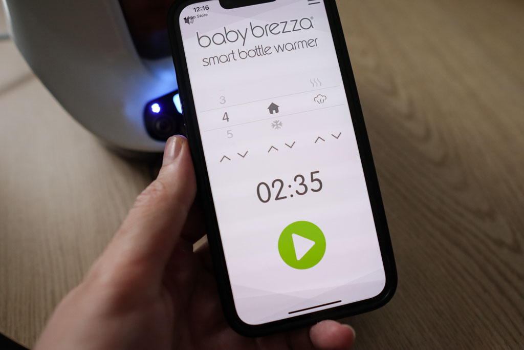 The Baby Brezza mobile app connected to the Smart Bottle Warmer, displaying warming controls on a smartphone screen.